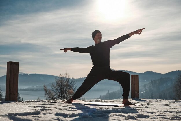 Kaukasischer älterer Mann, der Yogaübungen vor erstaunlichem Sonnenuntergang auf den Winterbergen tut