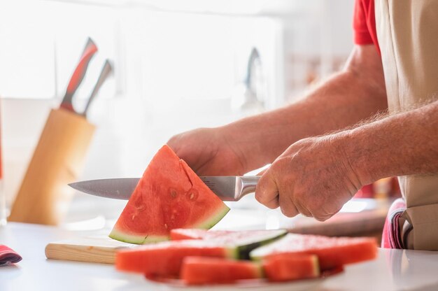 Kaukasischer älterer Mann in der Hauptküche beim Schneiden einer reifen roten Wassermelone in Scheiben