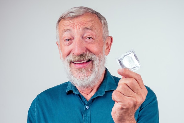 Kaukasischer alter älterer Mann, der verpacktes Gummilatexkondom im Studioweißhintergrund hält.