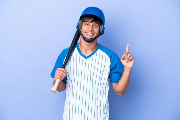 Kaukasischer Baseballspieler mit Helm und Schläger isoliert auf blauem Hintergrund, der einen Finger im Zeichen der Besten zeigt und hebt