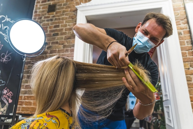 Kaukasischer Friseurmann mit einer Gesichtsmaske, der sich um den Schönheitssalon seiner Kunden kümmert