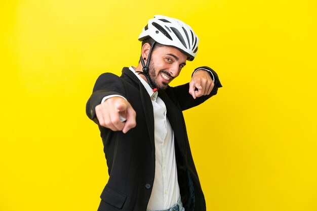 Kaukasischer Geschäftsmann mit einem Fahrradhelm, der auf gelbem Hintergrund isoliert ist, zeigt mit dem Finger auf Sie, während er lächelt