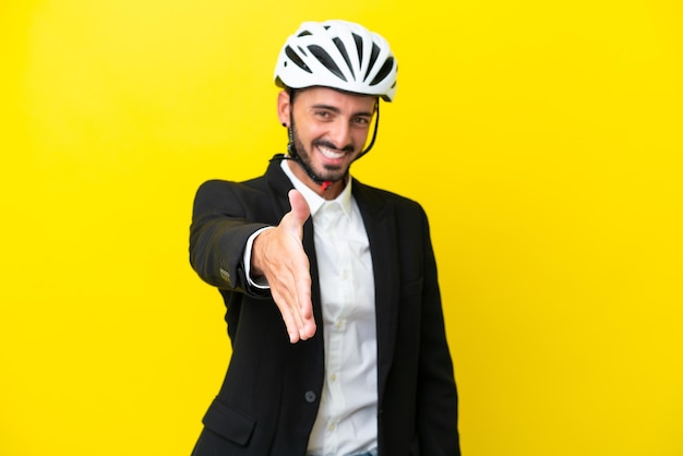 Kaukasischer Geschäftsmann mit Fahrradhelm isoliert auf gelbem Hintergrund, der sich die Hände schüttelt, um ein gutes Geschäft abzuschließen