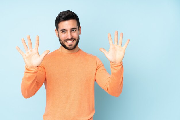 Kaukasischer gutaussehender Mann, der zehn mit den Fingern über der blauen Wand zählt