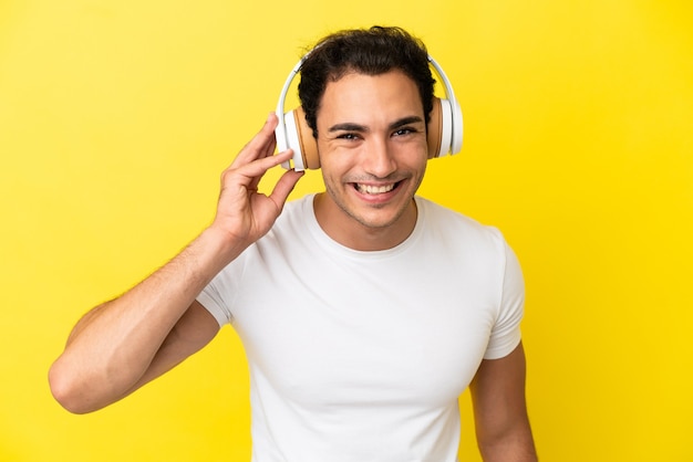 Kaukasischer gutaussehender Mann über isoliertem gelbem Hintergrund, der Musik hört