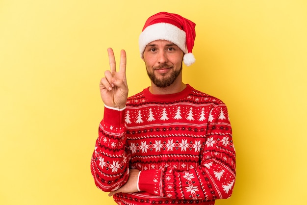 Kaukasischer Jüngling feiert Weihnachten isoliert auf gelbem Hintergrund, der Nummer zwei mit den Fingern zeigt.