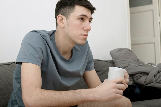 Kaukasischer Junge auf dem Sofa sitzt nach vorne mit einer Tasse Kaffee in der Hand