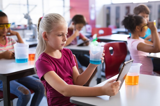 Kaukasischer Junge hält einen Becher in der Hand und nutzt ein digitales Tablet im Naturwissenschaftsunterricht im Labor