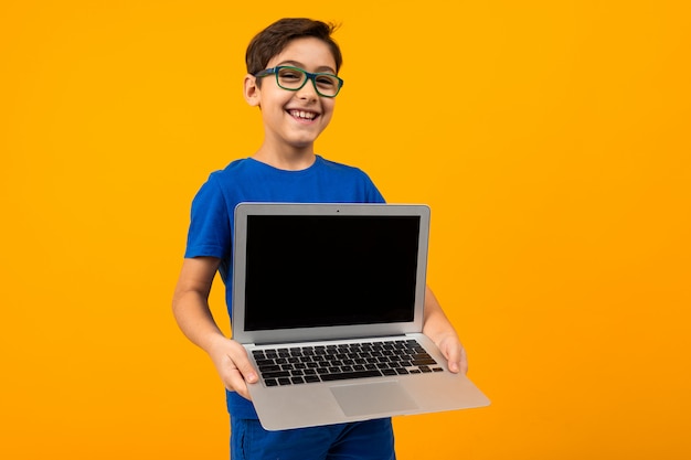Kaukasischer Junge hält Laptop-Bildschirm vorwärts mit Mock-up auf Gelb mit Kopierraum