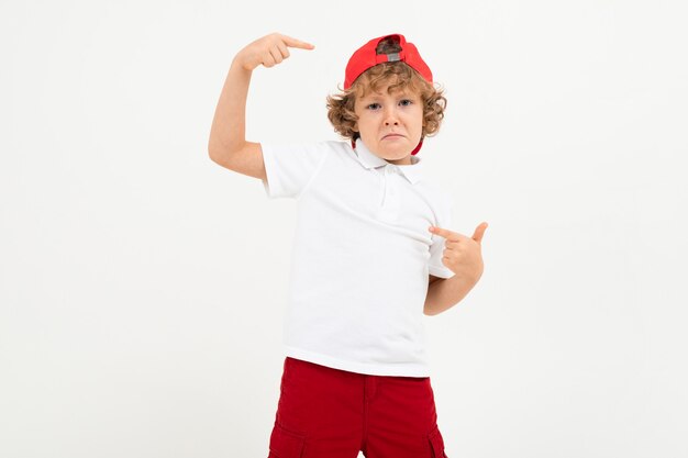 Kaukasischer Junge im weißen T-Shirt, rote Mütze, rote Shorts lächelt isoliert auf Weiß
