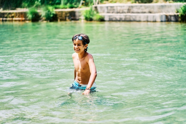 Kaukasischer Junge in Badeanzug und Taucherbrille, der im Sommer im Flusswasser lächelt