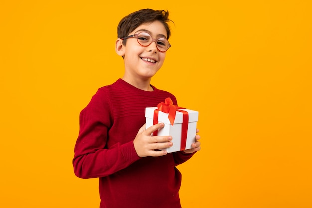 Kaukasischer Junge in einem roten Pullover mit einer Geschenkbox auf Gelb mit Kopienraum