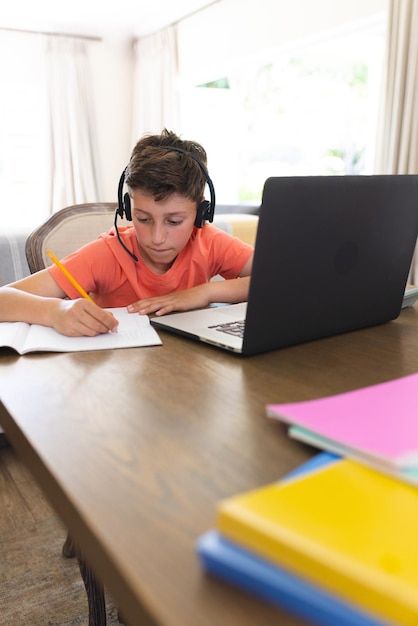 Kaukasischer Junge lernt und benutzt Laptop und Kopfhörer im Wohnzimmer