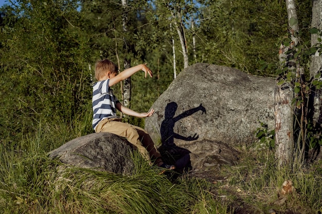 Kaukasischer Junge spielt Schattentheater auf einem großen Felsen im Wald