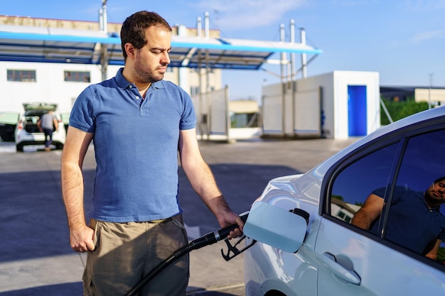 Kaukasischer junger Mann, der den Tank eines Kraftstoffautos an einer Tankstelle nachfüllt