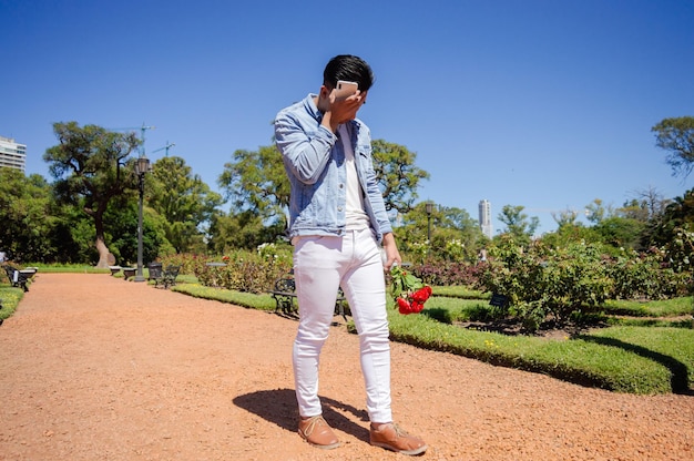 Kaukasischer junger Mann, der in einem Park mit einem Blumenstrauß und seiner Hand auf seinem Gesicht spaziert, traurig und enttäuscht von einem Lifestyle-Konzept mit gebrochenem Herzen