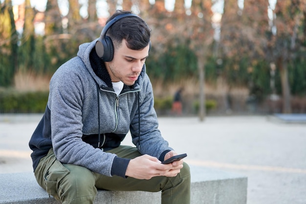 Kaukasischer junger Mann, der mit seinen Kopfhörern Musik im Park genießt