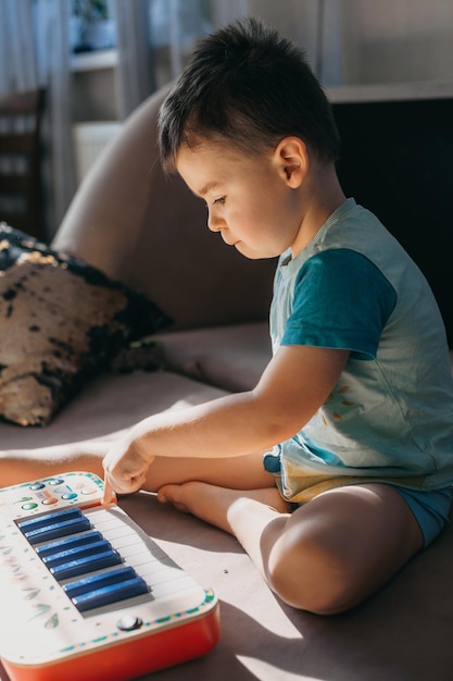 Kaukasischer kleiner Junge, der auf einem Bett sitzt und mit einem Plastikspielzeugmusikklavier-Bildungskonzept s spielt