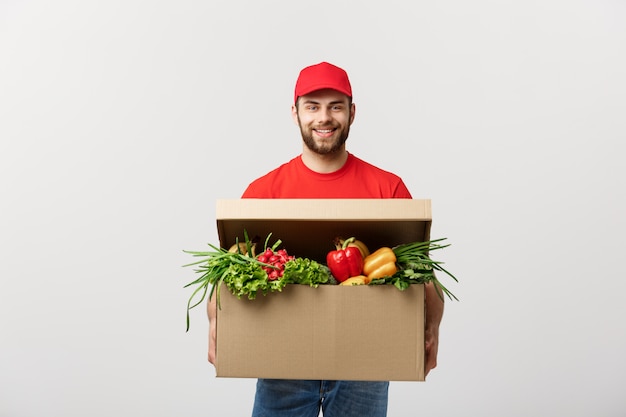 Kaukasischer Lebensmittelgeschäftlieferungs-Kuriermann in der roten Uniform mit Lebensmittelgeschäftkasten mit frischer Frucht