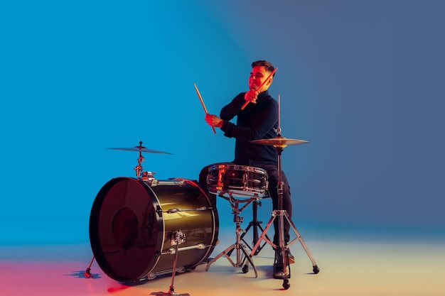 Kaukasischer männlicher Schlagzeuger improvisiert isoliert auf blauem Studiohintergrund im Neonlicht
