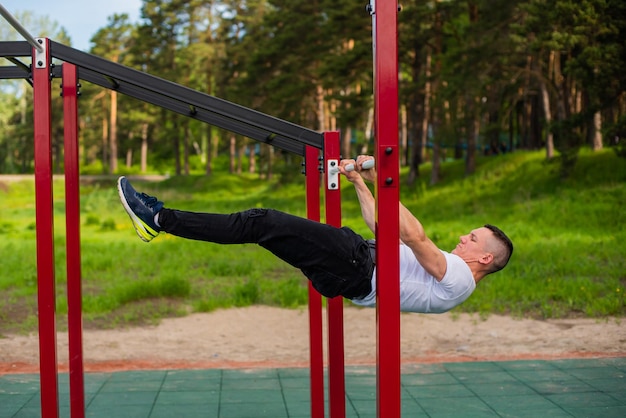 Kaukasischer Mann, der eine Rückenplanke auf den Stufenbarren macht Training auf dem Sportplatz