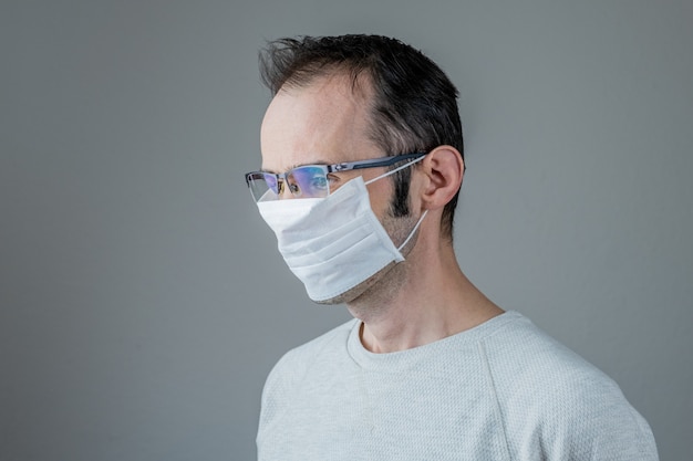 Kaukasischer Mann, der eine weiße medizinische Maske zum Schutz gegen ansteckende Krankheit, Coronavirus trägt