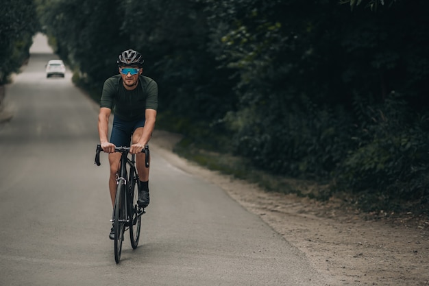 Kaukasischer Mann, der Fahrrad auf der Straße unter Wald reitet.