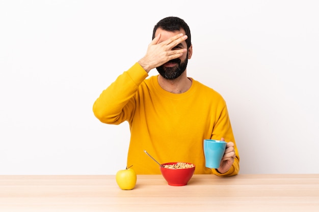 Kaukasischer Mann, der Frühstück in einem Tisch kegelt Augen durch Hände und Lächeln.