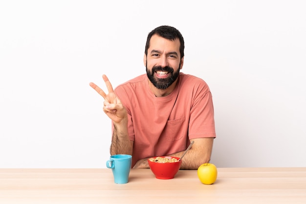 Kaukasischer Mann, der Frühstück in einem Tisch lächelt und Siegeszeichen zeigt.