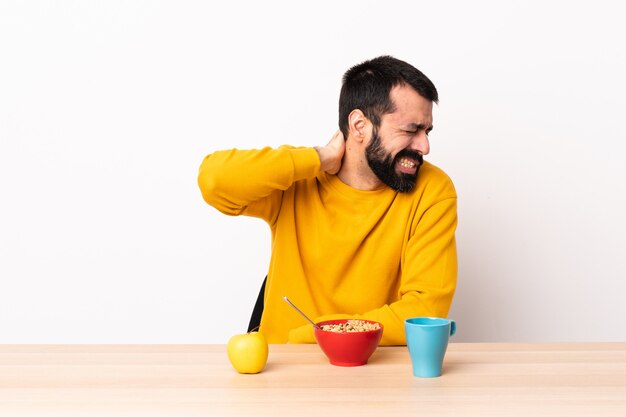 Kaukasischer Mann, der Frühstück in einem Tisch mit Nackenschmerzen hat