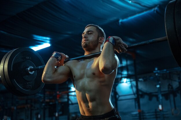 Kaukasischer Mann, der im Fitnessstudio Gewichtheben übt. Kaukasisches männliches sportliches Modelltraining mit Langhantel, sieht selbstbewusst und stark aus. Bodybuilding, gesunder Lebensstil, Bewegung, Aktivität, Aktionskonzept.