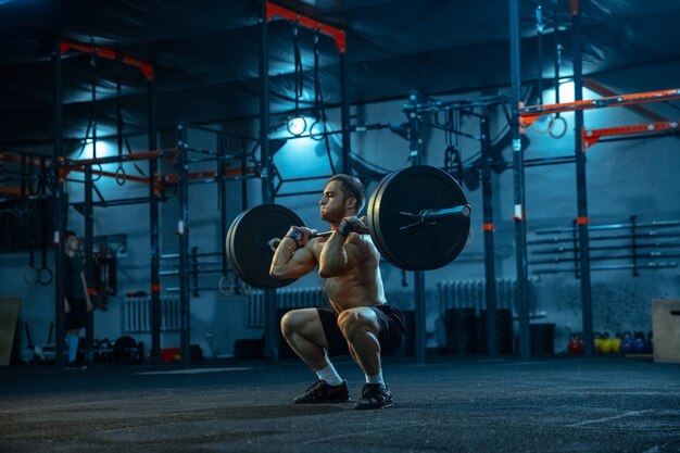 Kaukasischer Mann, der im Fitnessstudio Gewichtheben übt. Kaukasisches männliches sportliches Modelltraining mit Langhantel, sieht selbstbewusst und stark aus. Bodybuilding, gesunder Lebensstil, Bewegung, Aktivität, Aktionskonzept.