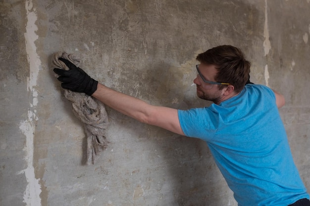 Kaukasischer Mann, der Wände mit altem Lappen von Staub wäscht