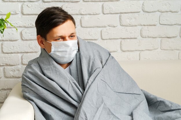 Kaukasischer Mann, der zu Hause während der Coronavirus / Covid-19-Quarantäne bleibt, die medizinische Maske trägt