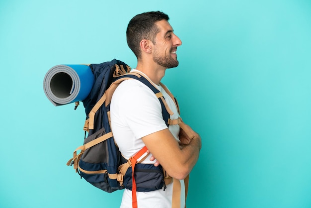 Kaukasischer Mann des jungen Bergsteigers mit einem großen Rucksack lokalisiert auf blauem Hintergrund in der seitlichen Position