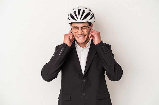 Kaukasischer Mann des jungen Geschäfts, der Fahrradhelm lokalisiert auf weißem Hintergrund hält, der Ohren mit den Händen bedeckt.