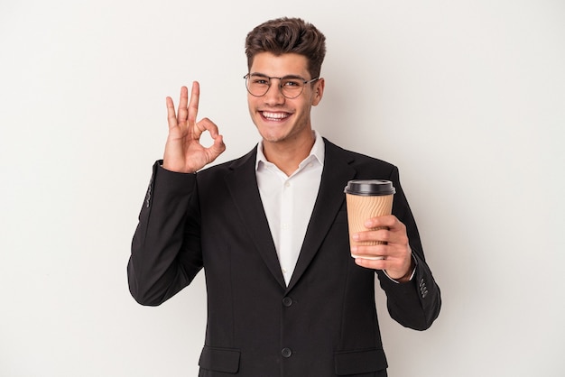 Kaukasischer Mann des jungen Geschäfts, der Kaffee zum Mitnehmen lokalisiert auf weißem Hintergrund hält, fröhlich und selbstbewusst, der ok Geste zeigt.