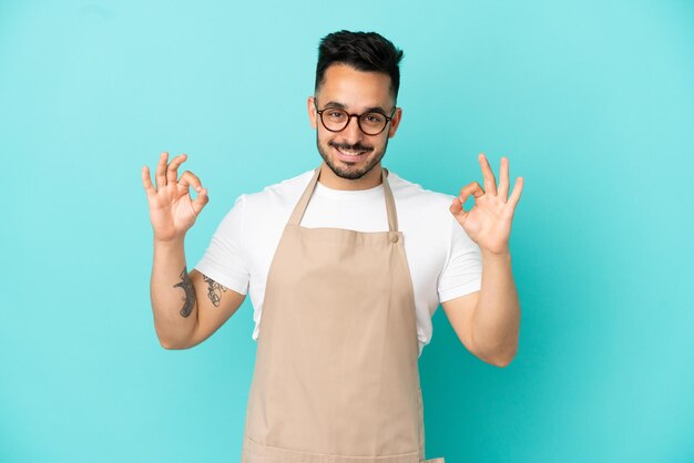 Kaukasischer Mann des Restaurantkellners lokalisiert auf blauem Hintergrund, der ein okayzeichen mit den Fingern zeigt