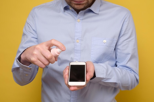 Kaukasischer Mann desinfiziert sein Smartphone, indem er ein Desinfektionsmittel aus einer Flasche sprüht