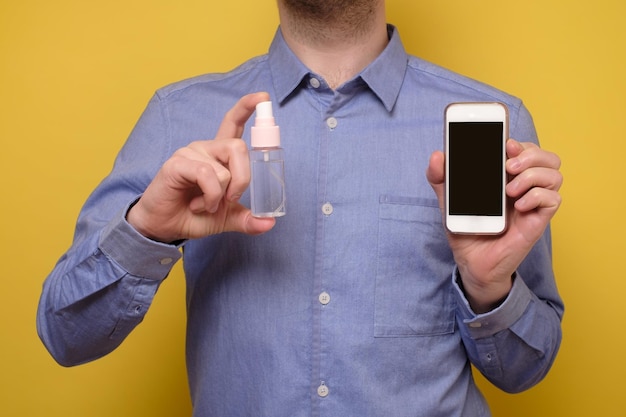 Kaukasischer Mann desinfiziert sein Smartphone, indem er ein Desinfektionsmittel aus einer Flasche sprüht