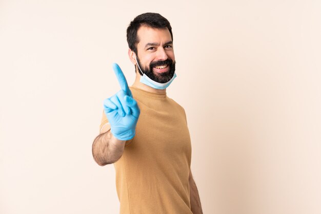 Kaukasischer Mann mit Bart, der mit einer Maske und Handschuhen über Wand schützt, die einen Finger zeigen und heben