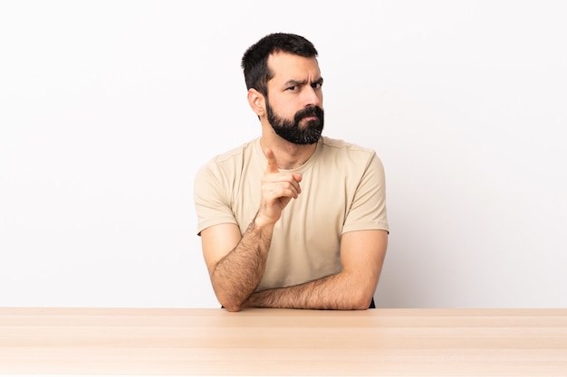 Kaukasischer Mann mit Bart in einem Tisch frustriert und nach vorne zeigend