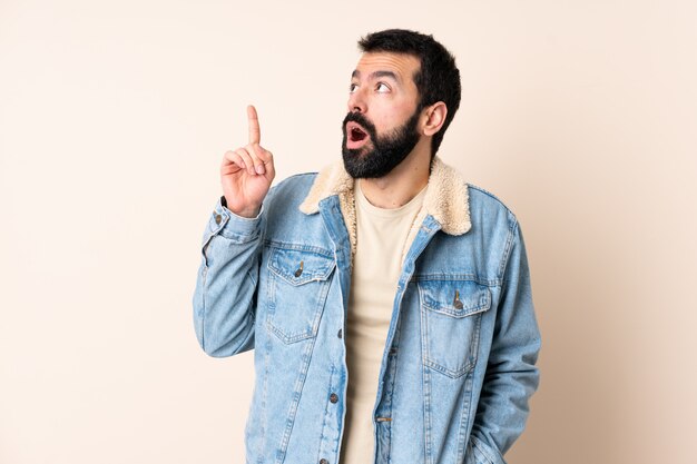 Kaukasischer Mann mit Bart über Wand, der eine Idee denkt, die den Finger nach oben zeigt