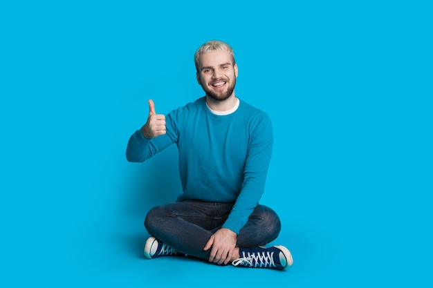 kaukasischer Mann mit blonden Haaren, die auf dem Boden im Studio sitzen und auf einer blauen Wand aufwerfen