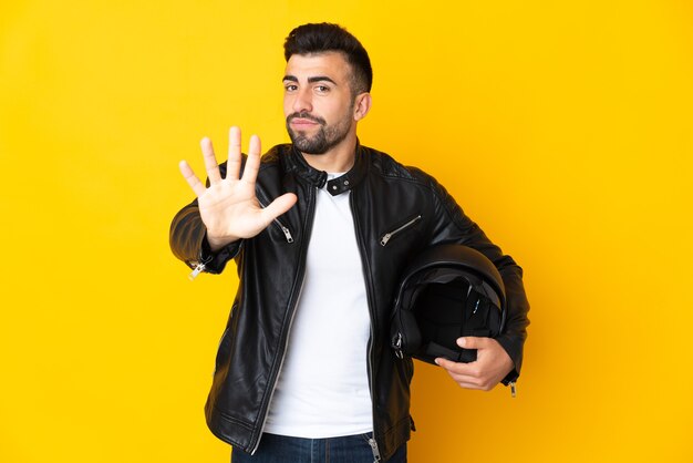 Kaukasischer Mann mit einem Motorradhelm über lokalisiertem gelbem Hintergrund, der fünf mit den Fingern zählt