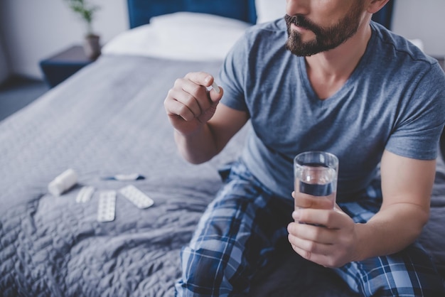 Kaukasischer Mann mit Pille und Glas Wasser auf dem Bett sitzend