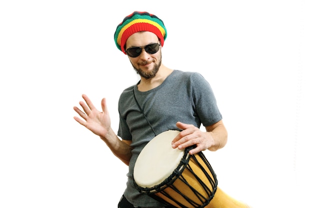 Kaukasischer Mann mit Rasta-Hut-Sonnenbrille und grauem T-Shirt auf weißem Hintergrund spielen auf Djembe-Trommel