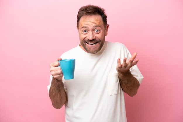 Kaukasischer Mann mittleren Alters, der eine Tasse Kaffee isoliert auf rosa Hintergrund mit schockiertem Gesichtsausdruck hält