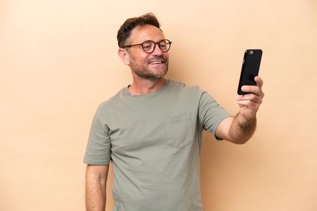 Kaukasischer Mann mittleren Alters isoliert auf beigem Hintergrund, der ein Selfie macht