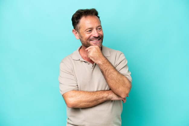 Kaukasischer Mann mittleren Alters isoliert auf blauem Hintergrund, der zur Seite schaut und lächelt